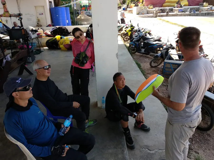 Instructor explaining a paraglider wing section to a group of students at launch