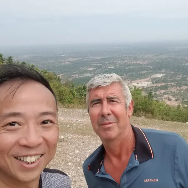 Two pilots at a hilltop take-off above a wide plain