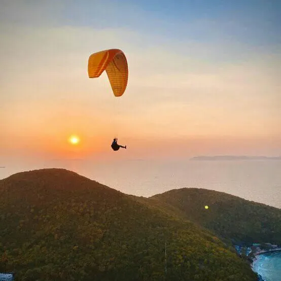 Paraglider over Koh Larn's hills at sunset with the pier and beach below